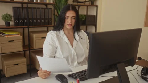 Woman working in an office holding documents, focusing on computer screen w.. Stock Footage 313856676