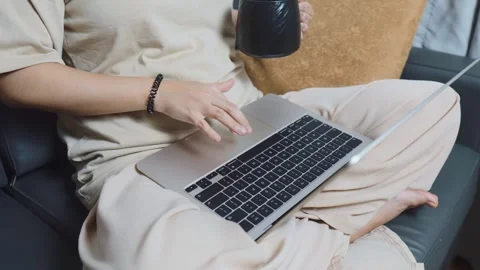 Woman working remotely from home, multitasking on laptop computer, holding a mug Stock Footage 334458892