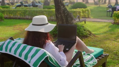 Woman working remotely on laptop while resting on sunbed at resort Stock Footage 291498161