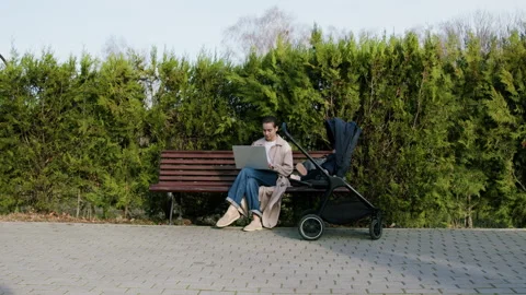 Woman working remotely on laptop while seated on a bench, surrounded by greenery Stock Footage 319338719