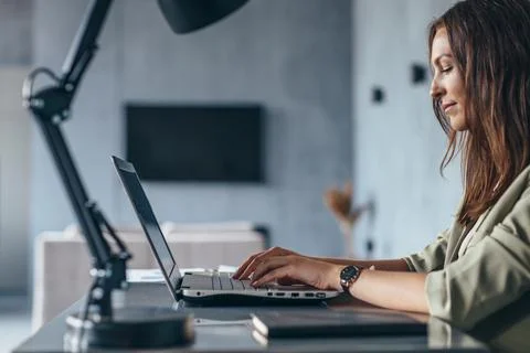 Woman works at home sitting at her desk with her laptop. Side view Stock Photos