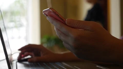 A woman works on a laptop while checking her smartphone at a cafe table Stock Footage 323809355