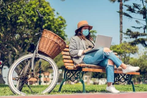 Woman works sitting in a park and protects herself with a medical mask. Portr Stock Photos