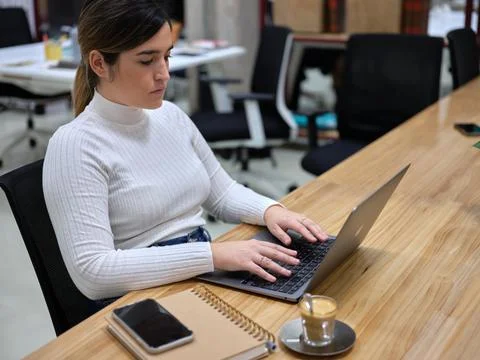 Woman in a workspace using her computer with a coffee next to it Stock Photos