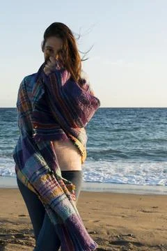 Woman wrapped in a blanket looking at the camera on the beach Stock Photos