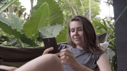 Woman write message on smartphone while sitting on hammock, natural background Video stock 84841960