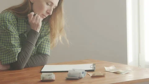 A woman writes leaning on a table. There is money on the table nearby. Home budg Video stock 233008237