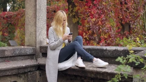 Woman Writes a Message on a Smartphone While Sitting on a Stone Bench in the Stock-Footage 71513681