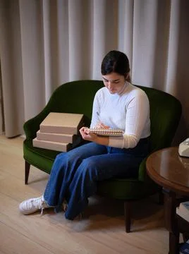 Woman writes a note of dedication to a client, sitting next to her product Stock Photos