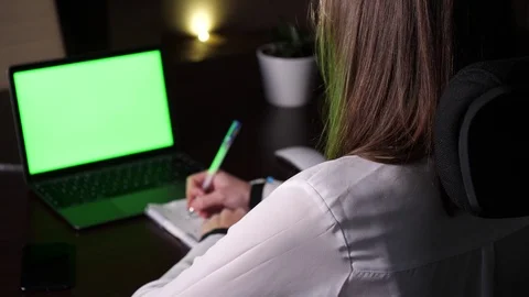 Woman writes notes in notebook in front of a laptop with green screen Video stock 101309504