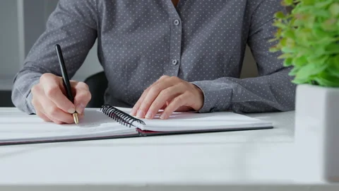 A woman writes notes by a pen in a notebook while sitting at the table. Stock Footage 160366537