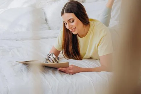 Woman writes in paper notebook with bionic arm lying on bed Stock Photos
