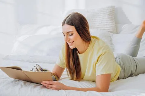 Woman writes in paper notebook with bionic arm lying on bed Stock Photos