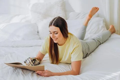 Woman writes in paper notebook with bionic arm lying on bed Stock Photos