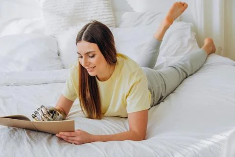 Woman writes in paper notebook with bionic arm lying on bed Stock Photos
