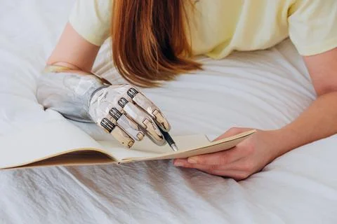 Woman writes in paper notebook with bionic arm lying on bed Stock Photos