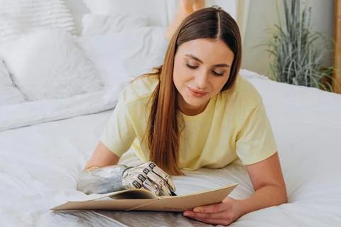 Woman writes in paper notebook with bionic arm lying on bed Stock Photos