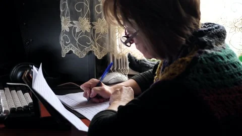 A woman writes with a pen in a notebook while sitting at a table. Stock Footage 332126143