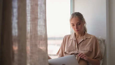 Woman writes report via computer sitting on sill at home Vídeo Stock 165826636