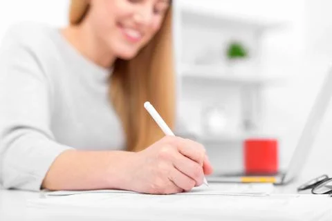 A woman writes while sitting at a table in an office or classroom. The girl Stock Photos