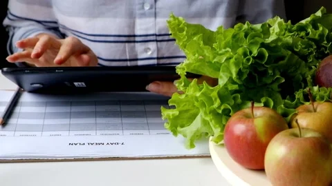 Woman writing diet plan using tablet PC on table full of fruits and vegetables Stock Footage 90753636