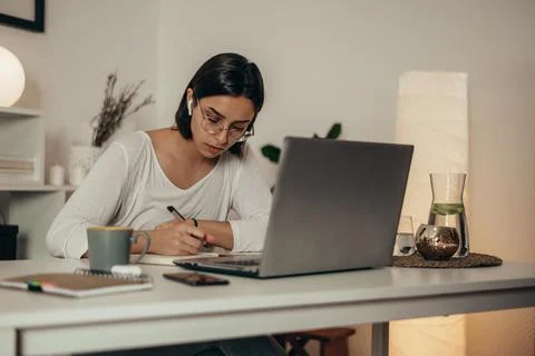 Woman writing in a notebook and using a laptop while working from home Stock Photos