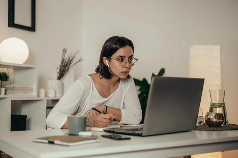 Woman writing in a notebook and using a laptop while working from home Stock Photos