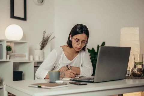 Woman writing in a notebook and using a laptop while working from home Stock Photos