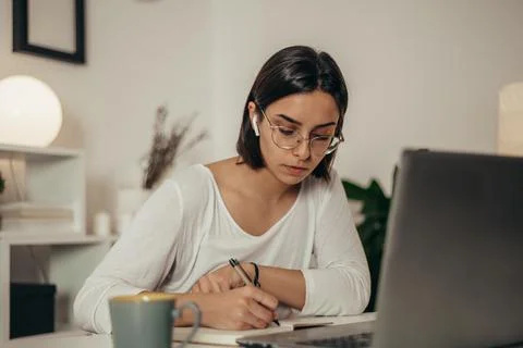 Woman writing in a notebook and using a laptop while working from home Stock Photos