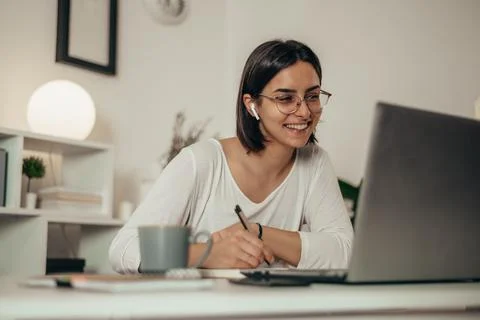 Woman writing in a notebook and using a laptop while working from home Stock Photos