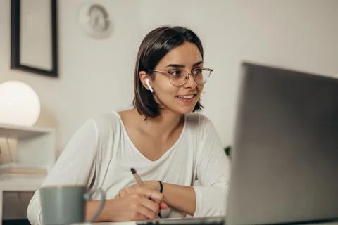 Woman writing in a notebook and using a laptop while working from home Stock Photos