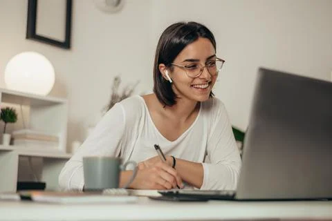Woman writing in a notebook and using a laptop while working from home Stock Photos