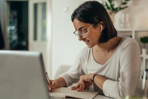 Woman writing in a notebook and using a laptop while working from home Stock Photos