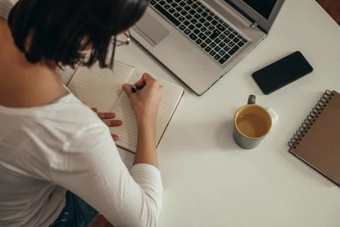 Woman writing in a notebook and using a laptop while working from home Stock Photos