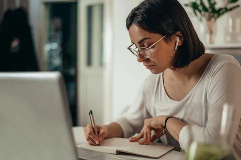 Woman writing in a notebook and using a laptop while working from home Stock Photos