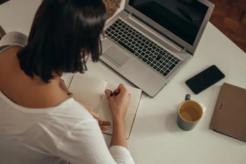 Woman writing in a notebook and using a laptop while working from home Stock Photos