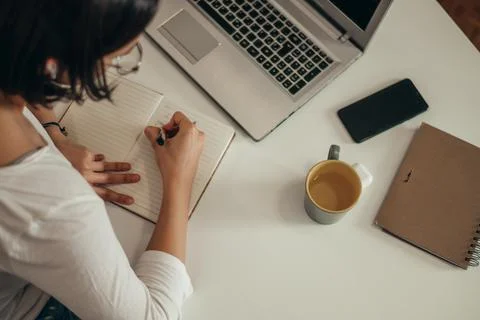 Woman writing in a notebook and using a laptop while working from home Stock Photos