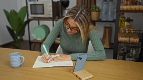 Woman writing in notebook at desk inside office with glasses and phone near.. Stock Footage 304620695