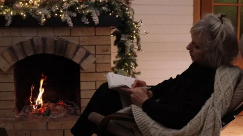 Woman writing in a notebook while sitting in an armchair by a burning fireplace. Stock Footage 326100959