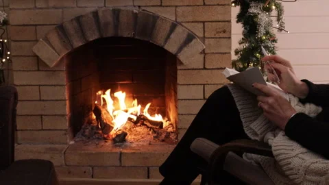 Woman writing in a notebook while sitting in an armchair by a burning fireplace. Stock Footage 326100983