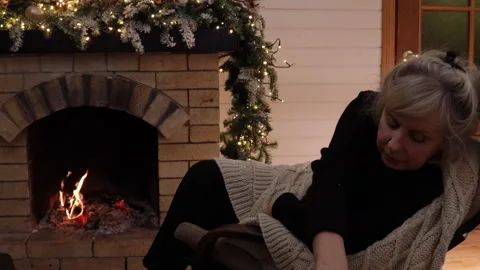Woman writing in a notebook while sitting in an armchair by a burning fireplace. Stock Footage 326101227