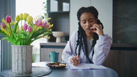 Woman writing in a notebook while sitting at a table with flowers and snacks in  Stock Footage 339321004