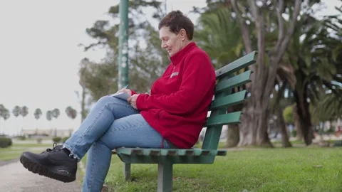Woman writing on notepad sitting on bench in park Stock Footage 309966932