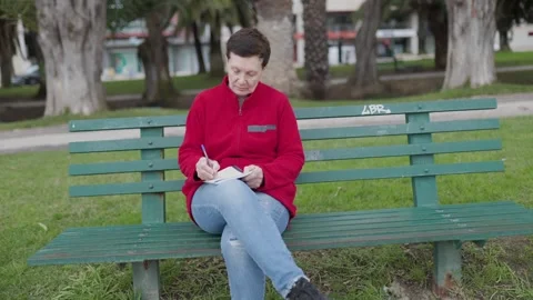 Woman writing notes on a bench in a park Stock Footage 309966918