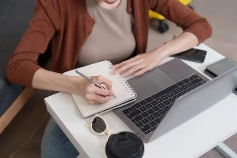 Woman writing notes in notebook next to laptop for remote work planning Stock Photos