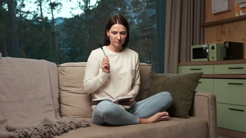 Woman writing notes in notebook sitting on sofa in living room Stock Footage 303498244