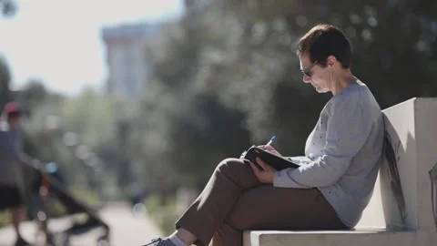 Woman writing notes in notebook sitting on bench in park Stock Footage 306292509