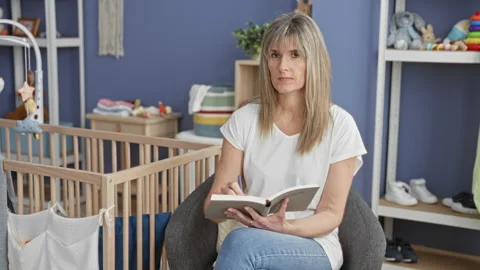 Woman writing notes in an open book while seated in an armchair beside a wo.. Stock Footage 337432415