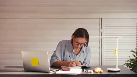 Woman writing notes talking on cellphone remote work from home office during Stock Footage 165459027