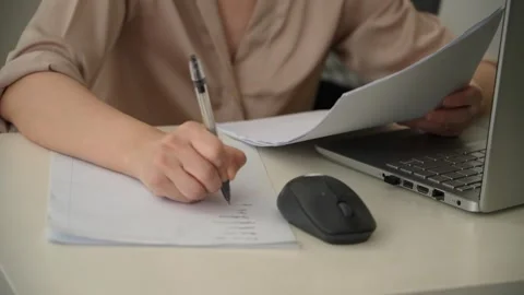 Woman Writing Notes While Reviewing Documents Beside Laptop. 스톡 동영상 344749133